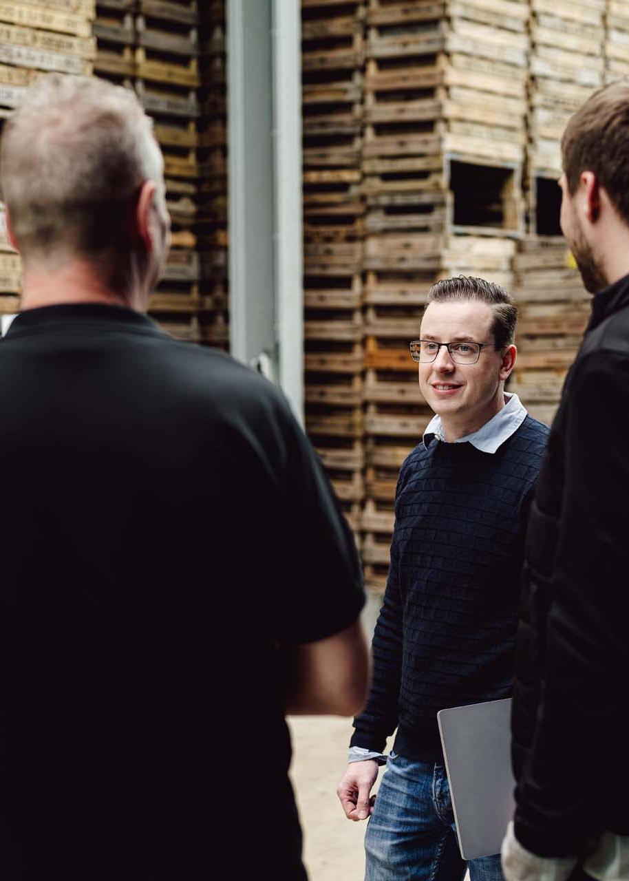 Consultant in gesprek met agrarisch ondernemers met pallets op de achtergrond.