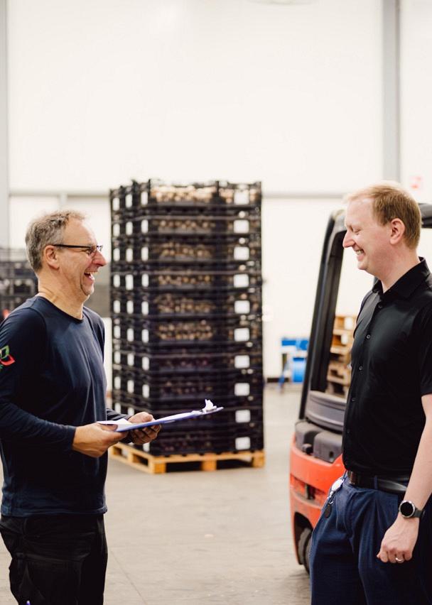 Twee personen in gesprek in een loods met heftrucks en karren vol bloembollenkratten.