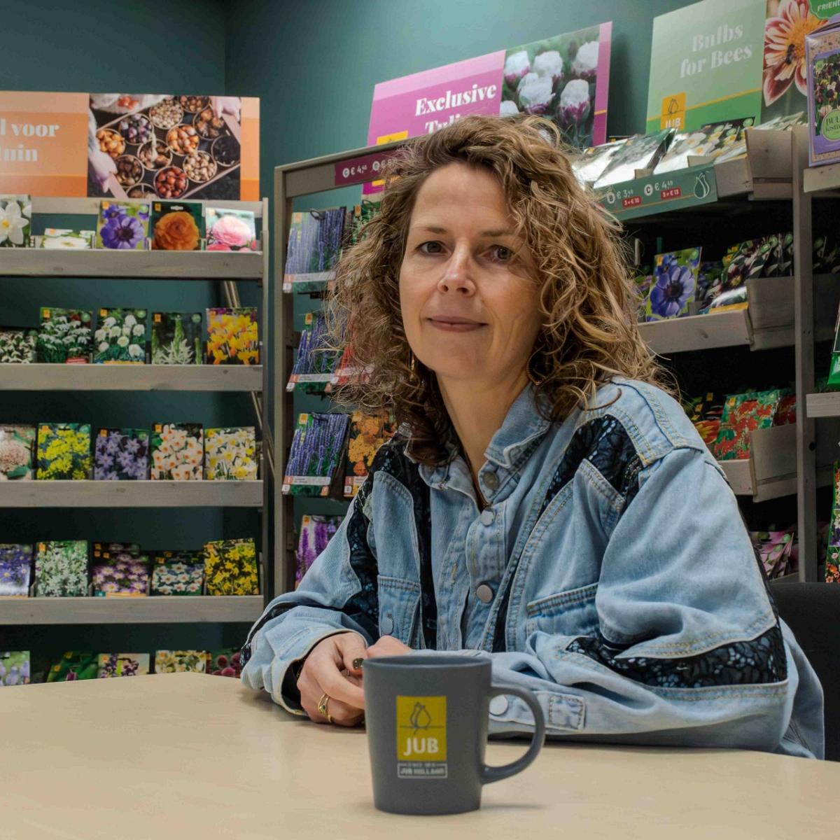 Vrouw aan tafel met JUB Bloembollen-mok, omringd door bloembollenverpakkingen.