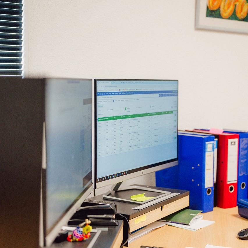 Bureauwerkplek met meerdere computerschermen, kantoorbenodigdheden en ordners in een nette kantoorruimte.
