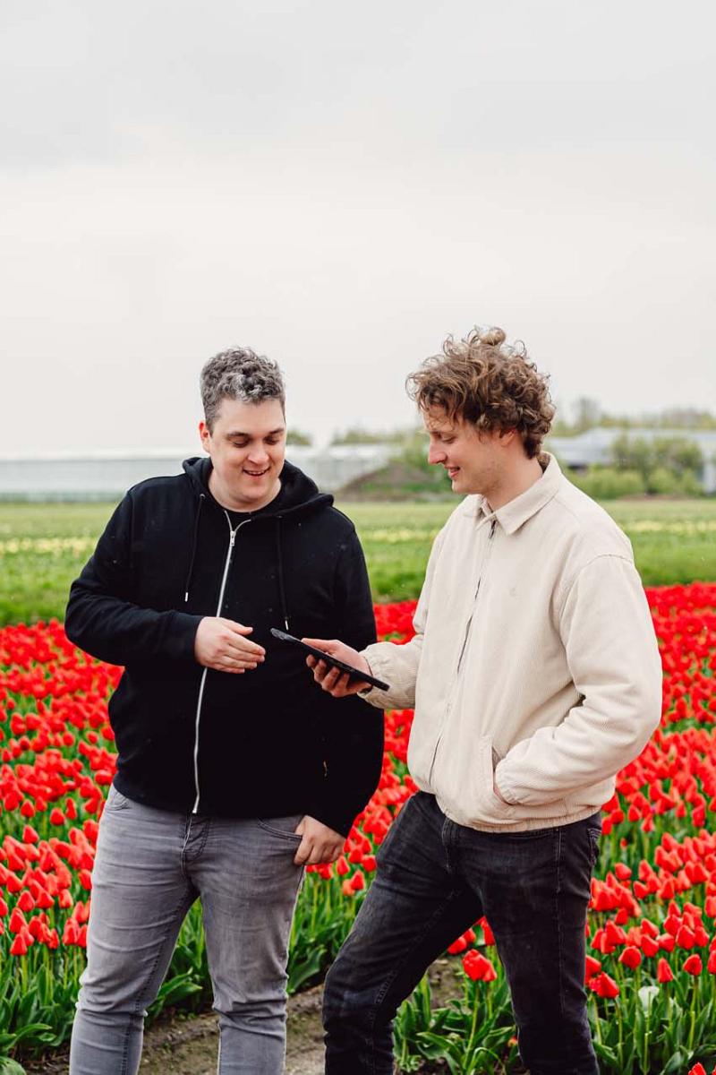 Smart Bulb consultant met kweker bij een bloemenveld in gesprek en kijkend op een tablet.