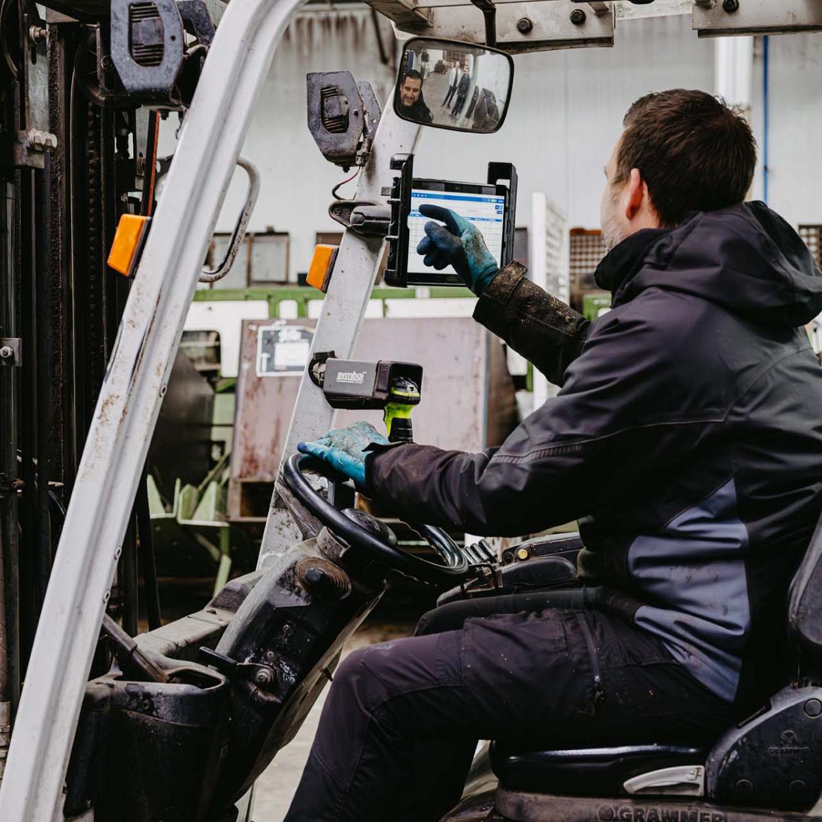 Man in heftruck tikt iets aan op het scherm van een tablet.
