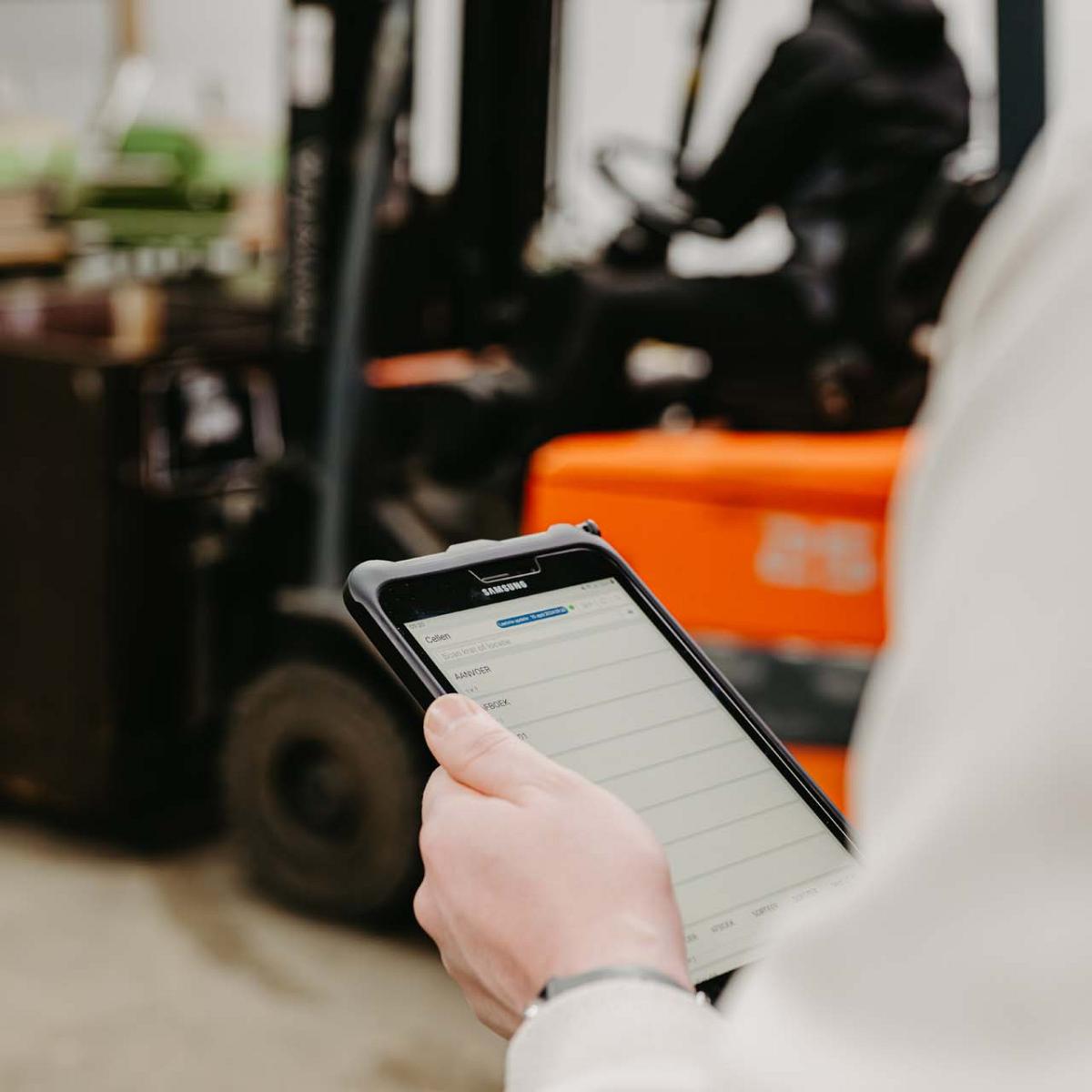 Man staat bij lopende band met tulpenbollen kijkend op mobiel in zijn hand.