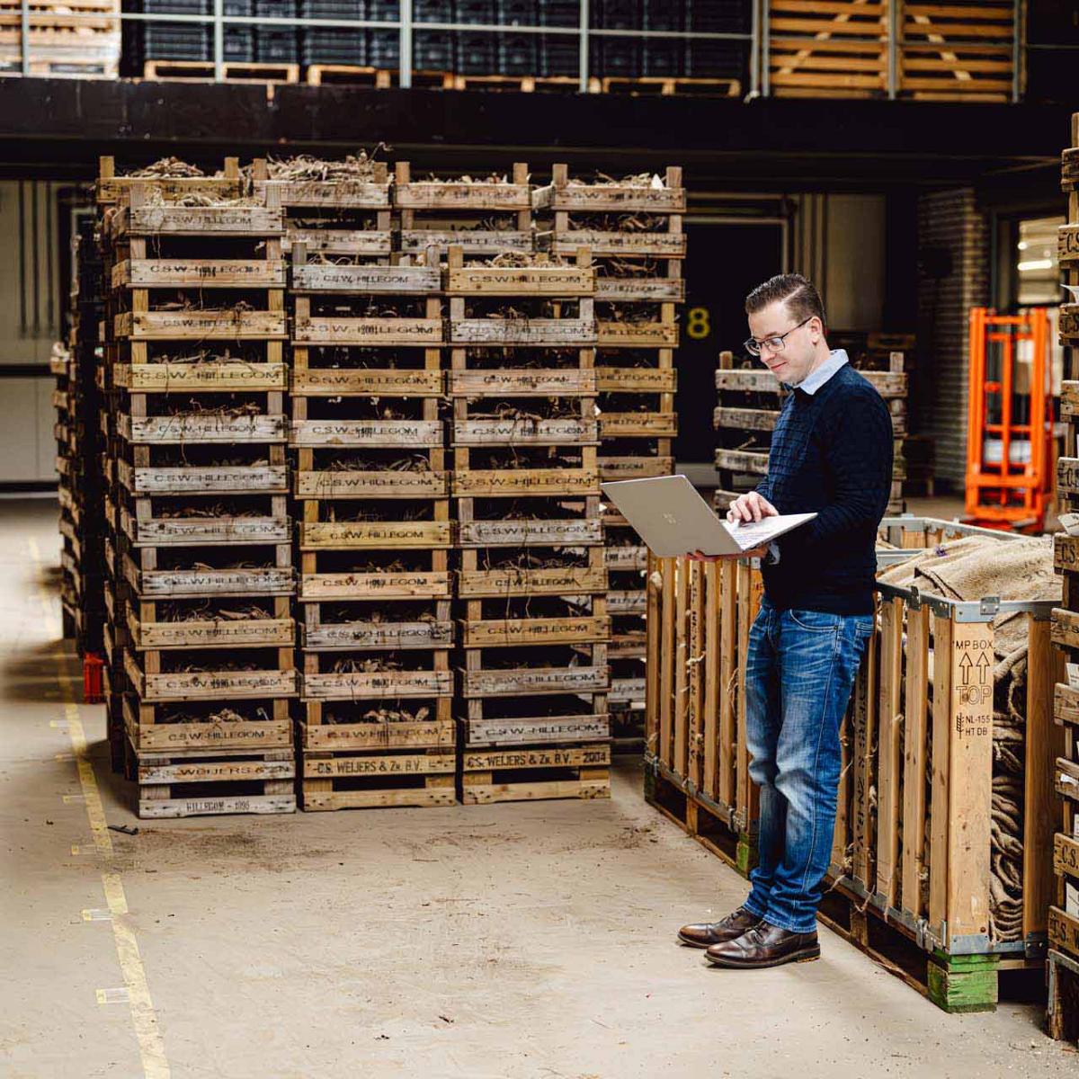 Smart Bulb consultant staat tegen kist met laptop in bollenschuur.