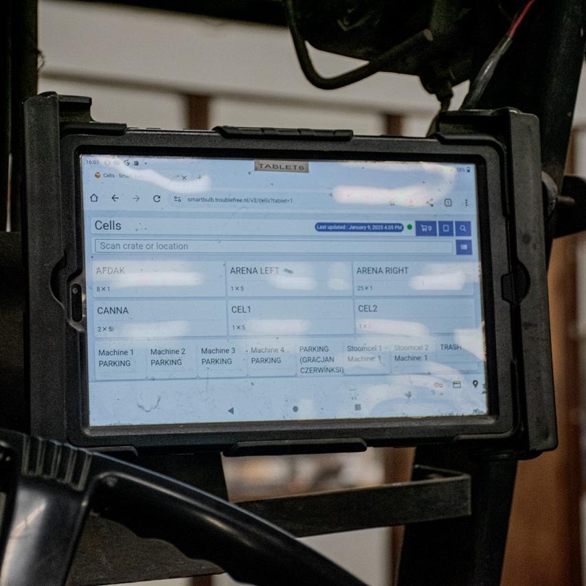 Tablet gemonteerd in een heftruck, met een scherm dat een overzicht toont van locaties en cellen. Op de achtergrond een magazijnruimte met houten wanden.
