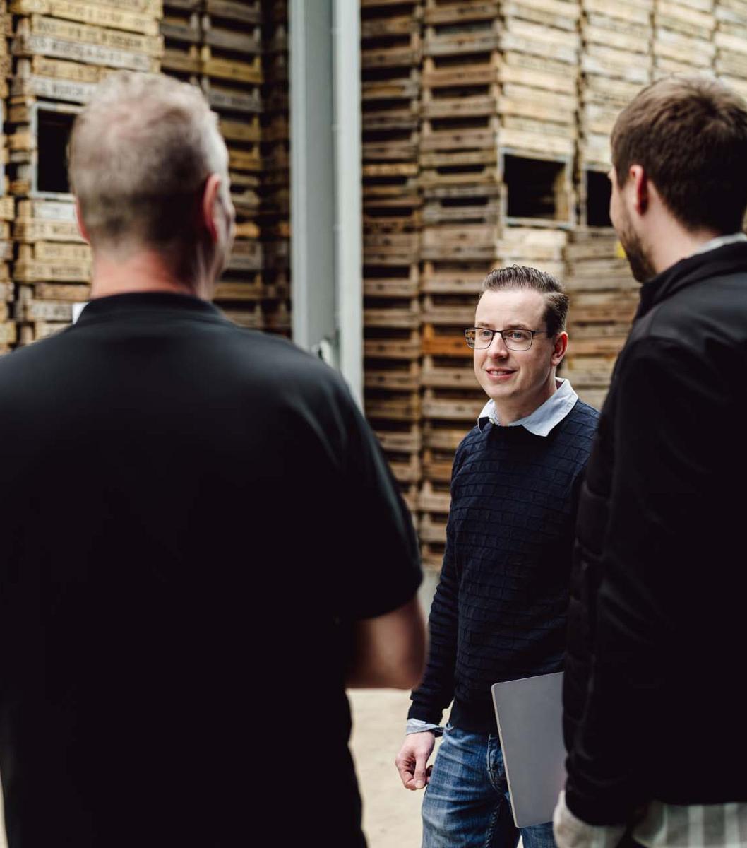 Drie mannen staan te praten met op de achtergond houten bloembollenkratten.